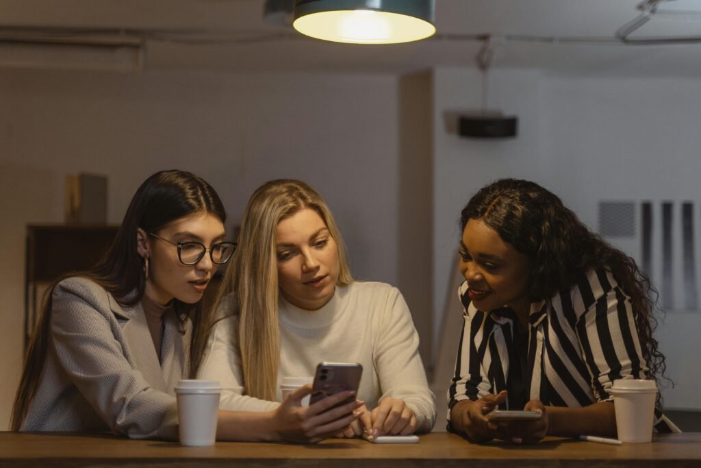 Why Mutual Respect is Important in Casual Hookups 4 Three diverse women enjoying time together, interacting with smartphones at a table indoors.