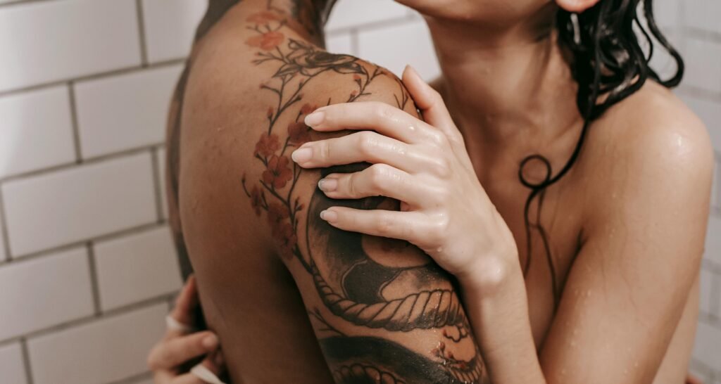 How to Fight Casual Sex Stigma and Avoid Succumbing to Shaming 4 A close embrace in the shower, revealing tattoos and intimacy.