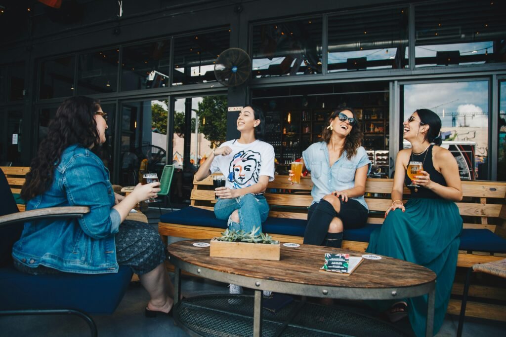 Alcohol and Casual Sex – Having Fun But Remaining Safe 4 Four friends laughing and enjoying drinks together at an outdoor cafe setting, reflecting happiness and camaraderie.