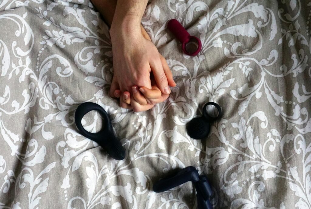 Alcohol and Casual Sex – Having Fun But Remaining Safe 3 Intimate scene with hands holding on a patterned bedspread with adult toys.